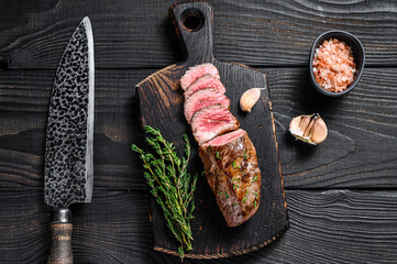 Grilled lamb tenderloin meat steak  on a meat cleaver. Black wooden background. Top view