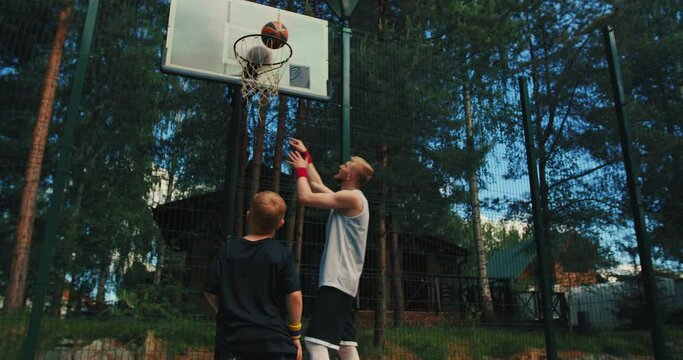 Male basketball instructor training boy player scoring hoop throwing ball in basket on basketball court outdoors
