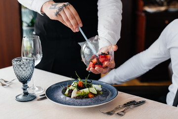 The waiter makes an exquisite serving of seafood salad, tuna and black caviar in a beautiful serving on the table in the restaurant. Exquisite delicacies of haute cuisine close-up.
