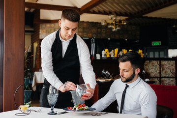 The waiter makes an exquisite serving of seafood salad, tuna and black caviar in a beautiful serving on the table in the restaurant. Exquisite delicacies of haute cuisine close-up.