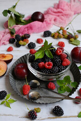 Vertical composition. Juicy raspberries, blackberries, plums and leaves on plates on a light background. Closeup