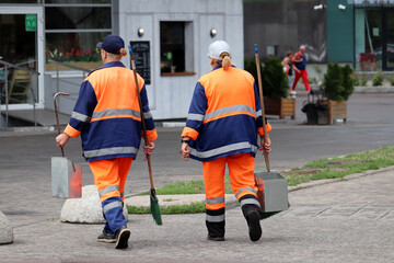 Two female janitors walking on the street. Cleaning city at summer, women with brooms