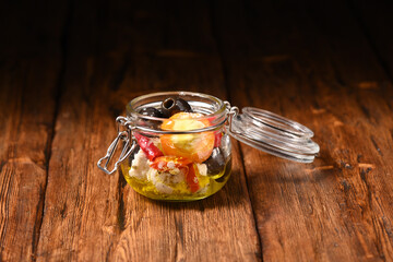 Feta cheese, pickled peppers and olives in a storage jar on the wooden table.