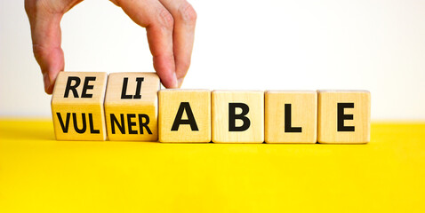 Vulnerable or reliable symbol. Businessman turns wooden cubes and changes the word Vulnerable to...