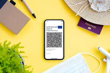 An aircraft model, sun hat, face mask, passport and a smartphone with the Green Pass, are arranged on a yellow background. 