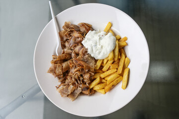 Doner kebab meat slices from rotating roasting spit with french fries and tzatziki yoghurt dip, served on a white plate in a turkish fast food restaurant, copy space, view from above