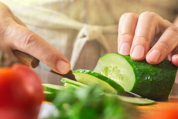 Chef slicing cucumber on the table in restaurant. Process of cutting vegetables in kitchen.