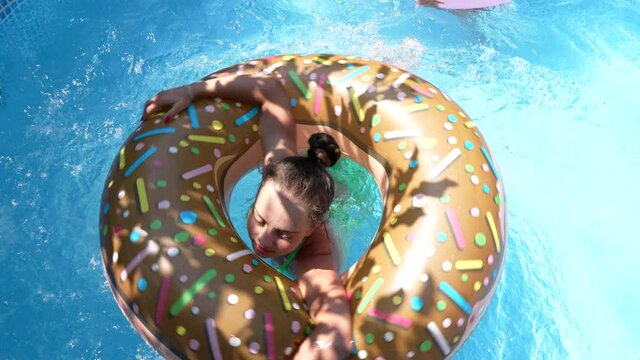 Girl child swim in donut pool float in outdoor swimming pool on sunny summer day, floatation