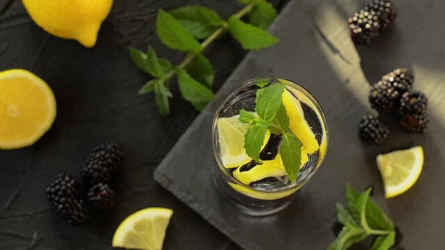 Refreshing bramble and mint mojito cocktail in a glass on black stone table. Decorated a glass cold lemonade with mint leaf. Summer mint and lemon refreshing healthy drink. Top view.