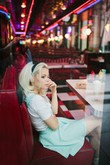 Blonde adorable female in retro cafe sitting and look into the camera