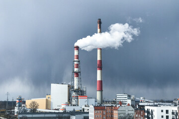 Thick white smoke comes out of a large chimney of an industrial facility or factory. Chimney...