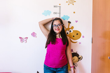 Hispanic teen girl with down syndrome measuring her height on the wall, in disability concept in Latin America