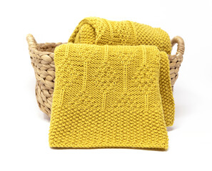 Yellow knitted blanket in diamonds pattern in basket on white background