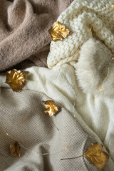 Pile of knitted clothes with autumn gold leaves, warm background, knitwear, space for text, Autumn winter concept.