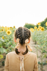 Fototapeta premium Local travel. Six year girl wearing natural linen dress pastel color in sunflower field at summer, outdoor lifestyle. Freedom concept