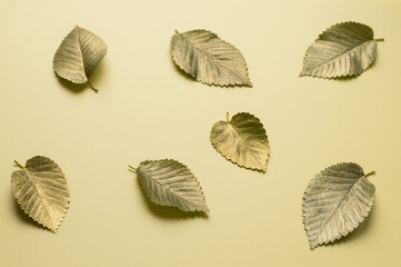 Leaves in gold paint on a yellow background. Autumn concept. Top view of autumn leaves in gold paint on beige with copy space for your text to the right.