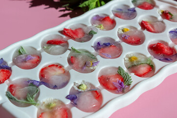 Edible flowers, strawberries and mint in an ice cube tray.