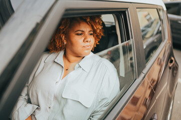 Happy young smiling African American woman red afro haired driver sitting in new brown car, smiling looking at camera enjoying journey. Driving courses and life insurance concept.