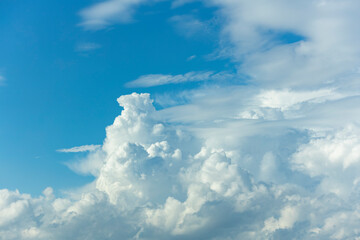 Towering water filled cumulonimbus rain cloud contrasted against a vibrant blue sky rising up and lit up brightly from the side. Weather conditions and climate detail background.