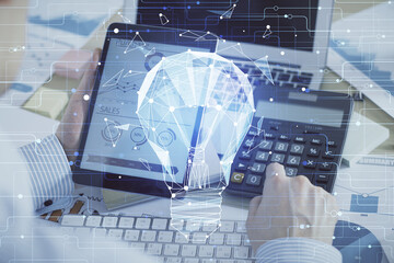 Double exposure of man's hands holding and using a digital device and bulb hologram drawing. Idea concept.