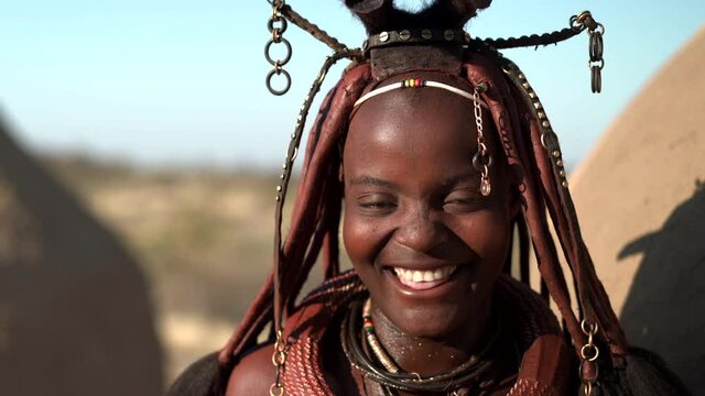 Happy young Himba woman smiling, wearing traditional jewellery and headdress in her village near Kamanjab in northern Namibia, Africa.