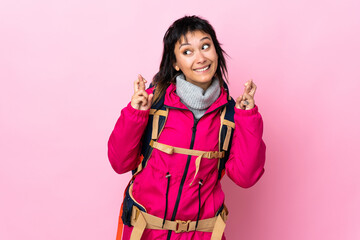 Young mountaineer girl with a big backpack over isolated pink background with fingers crossing