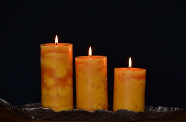 three large wax candles in a metal candlestick on a black background 