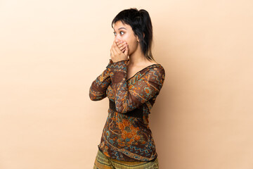 Indian woman isolated on beige background covering mouth and looking to the side