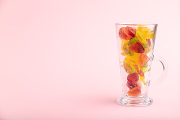 Various fruit jelly candies in drinking glass on pink background. copy space, side view.