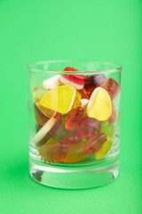 Various fruit jelly candies in drinking glass on green background. close up, side view.