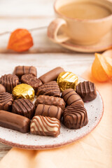 Chocolate candies with cup of coffee and physalis flowers on a white wooden background. side view, selective focus.