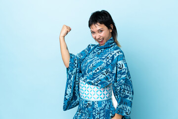 Young woman wearing kimono over isolated blue background celebrating a victory