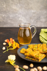 Traditional iranian dessert sohan with glass of green tea on a black concrete background. side view, close up.
