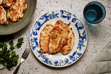 Plate with cooked marinated chicken breast fillets on a granite table
