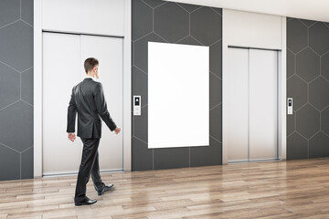 Fototapeta na wymiar Businessman walking in modern office lobby interior with steel elevators, empty white poster, wooden flooring and tile wall. Mock up.