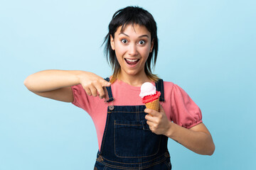Young Uruguayan girl holding a cornet ice cream over isolated blue background surprised and pointing front