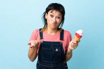Young Uruguayan girl holding a cornet ice cream over isolated blue background making doubts gesture...