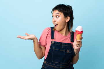 Young Uruguayan girl holding a cornet ice cream over isolated blue background with surprise facial...