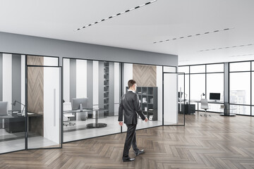 Business man walking in modern concrete glass office interior with daylight, equipment and wooden flooring. Workplace design concept.