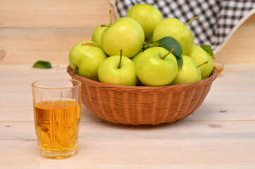 a glass of apple juice and a basket of apples on the table