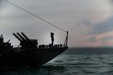 Silhouettes of a crowd standing at blurred military war ship on foggy background. Selective focus.