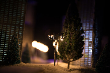 Little miniature city with road and lights. Decorative cute small houses in snow at night in...