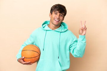 Handsome young basketball player man isolated on ocher background smiling and showing victory sign