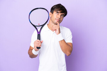 Handsome young tennis player man isolated on ocher background having doubts while looking up
