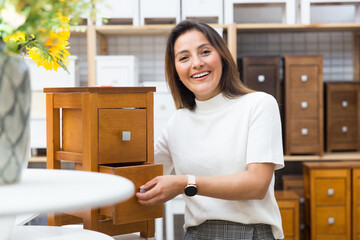 Portrait of a positive hispanic female customer choosing wooden commode in decor items store