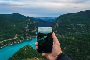 hand holding mobile phone with camera on and natural landscape in the background