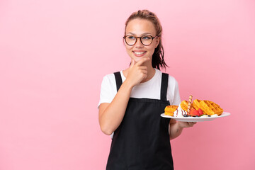 Restaurant waiter Russian girl holding waffles isolated on pink background looking to the side and smiling