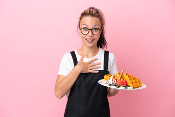 Restaurant waiter Russian girl holding waffles isolated on pink background surprised and shocked while looking right