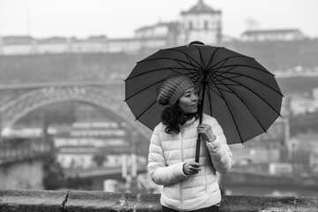 Multicultural woman with an umbrella in cloudy weather in Porto, Portugal. Black and white photo.