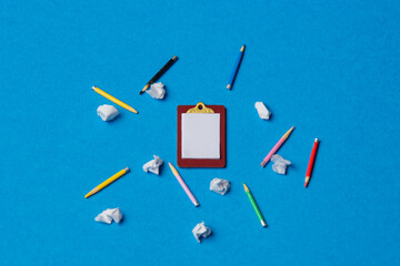 Board and pencils with crumpled papers on blue background